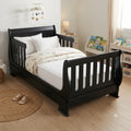 A black wooden toddler bed with a slatted headboard and footboard, styled with white bedding and a patterned duvet in a bright children's bedroom.