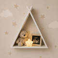 A white triangular shelf mounted on a beige wall with cloud and star decals, styled with a teddy bear, a framed ultrasound photo, and a glowing star night light.