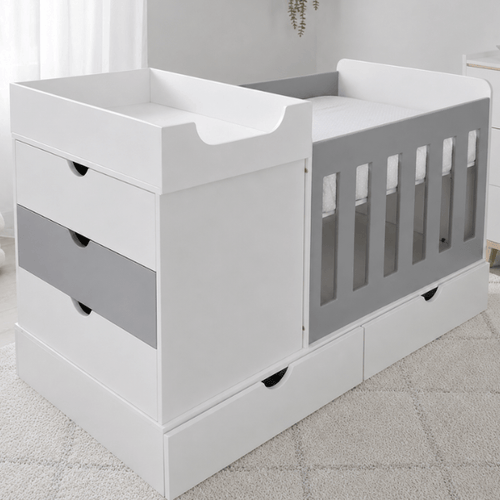 White and gray convertible toddler bed with built-in changing tray and storage drawers, shown in a softly lit nursery setting.