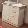 White baby changing table with drawers and a gray cover on a brown floor.