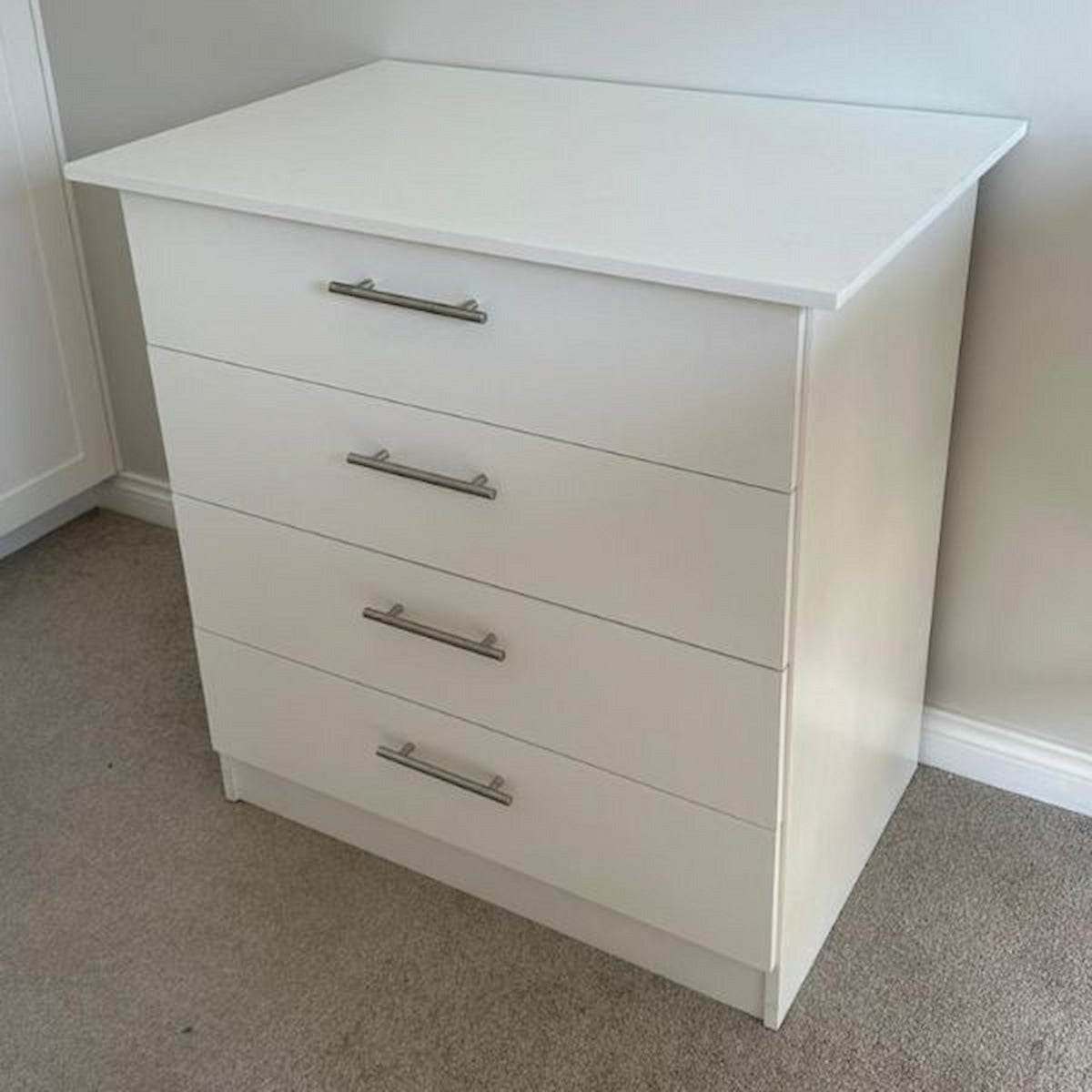 White dresser with four drawers in a room with beige carpet and white walls.