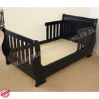 SleighCot-Convertsinto3.4Bed Black wooden crib on a beige floor with a plain background