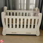 Hurricane Cot White crib with slatted design on a wooden floor with curtains in the background