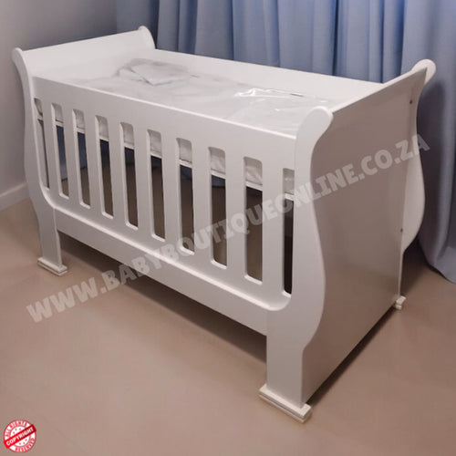 2in1 Sleigh wooden Cot White baby crib in a room with light blue curtains.