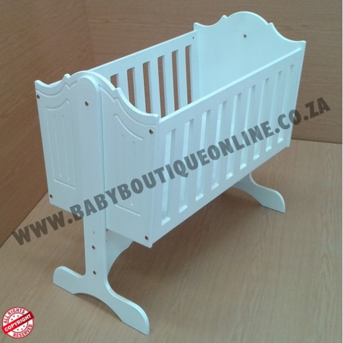 White baby crib on a wooden floor with 'www.babyboutiqueonline.co.za' branding.
