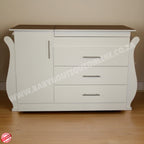 White dresser with brown top on a wooden floor against a beige wall.