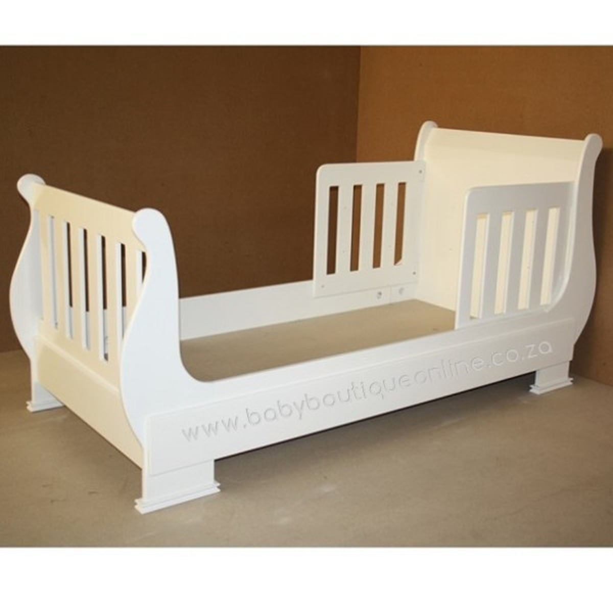 White toddler bed with beige mattress on a brown background