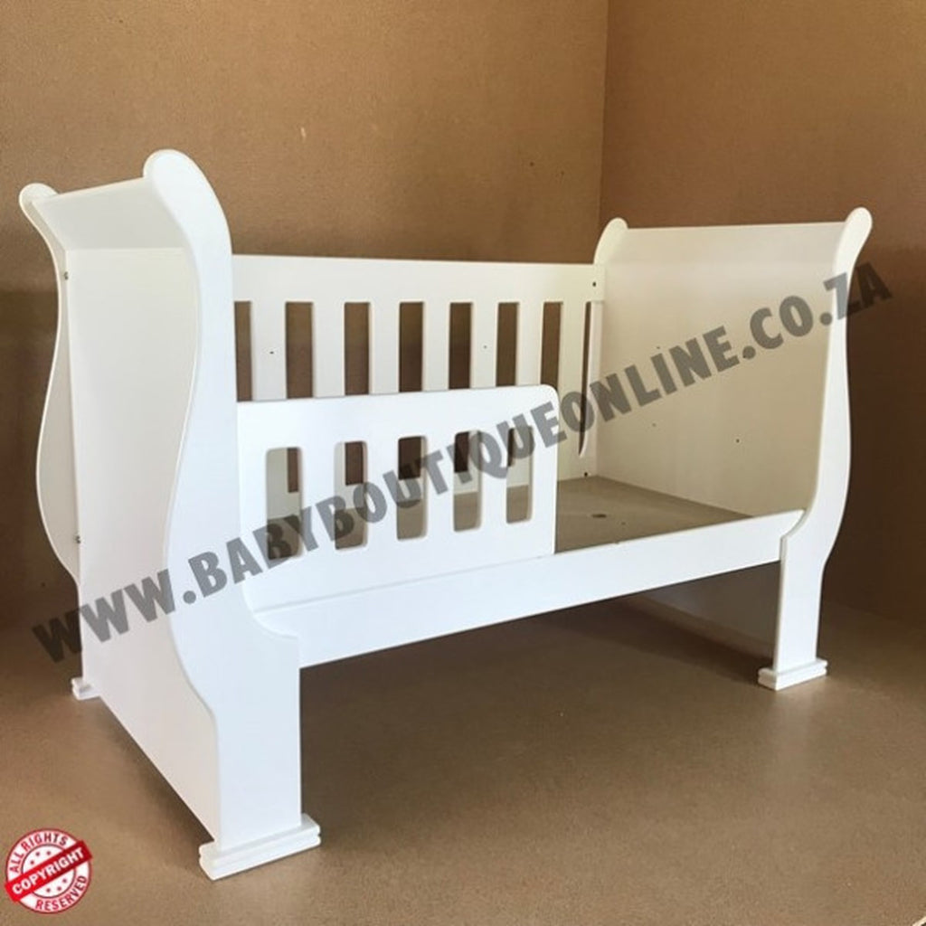 3-in-1 Sleigh Cot and Co-Sleeper White baby crib on a wooden floor with white curtains in the background White crib on a brown background with 'www.babypoutiqueonline.co.za' text.