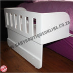 White co sleeper with purple bedding on a wooden floor, featuring a visible brand name.