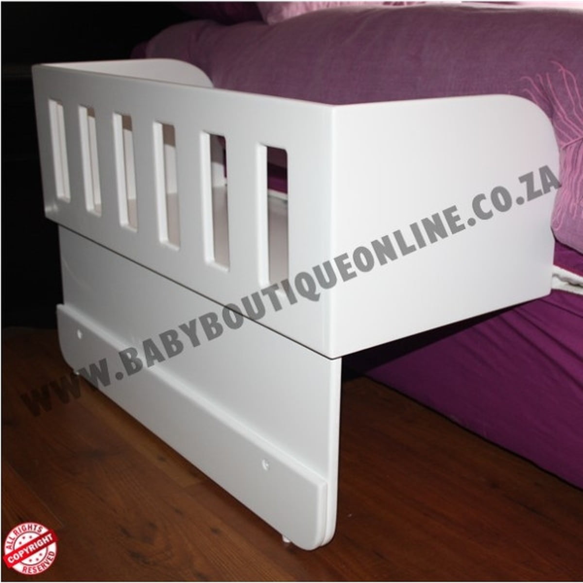 White co sleeper with purple bedding on a wooden floor, featuring a visible brand name.