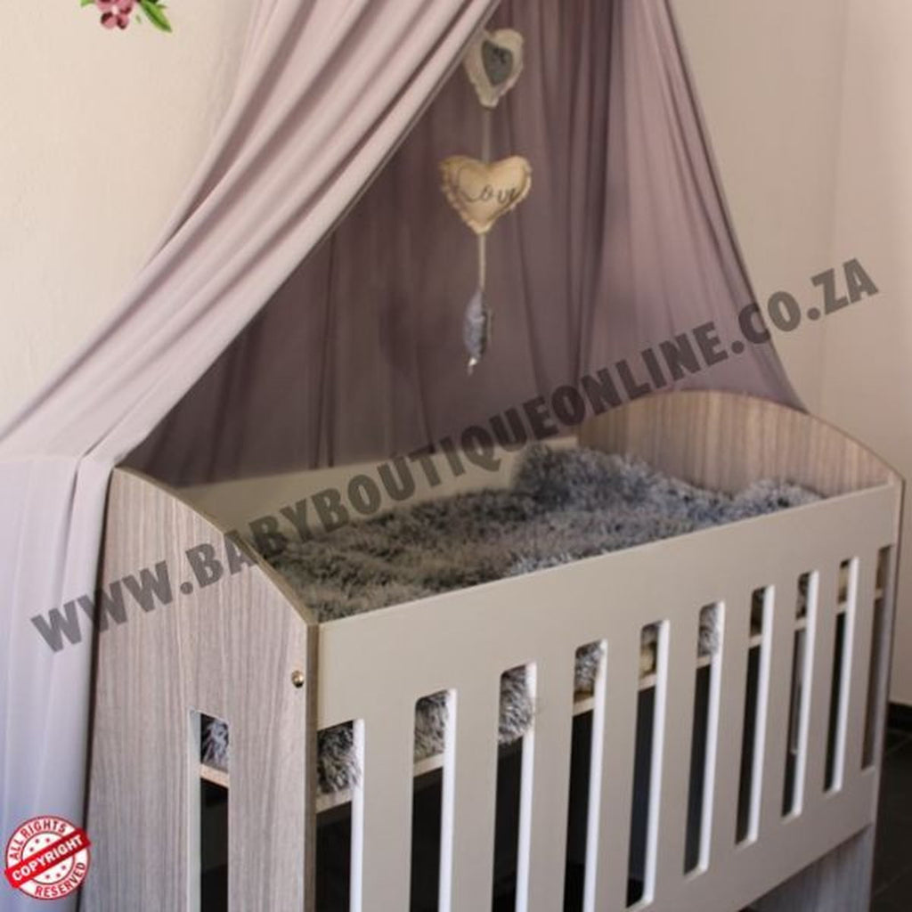 Large Wooden Cot-Round Sides Wooden crib with a canopy in a room setting, featuring a brand logo.
