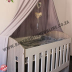 Large Wooden Cot-Round Sides Wooden crib with a canopy in a room setting, featuring a brand logo.