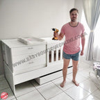 Man holding a power drill in front of baby furniture Babybedroominabox5-in-1Cot with 'www.babyboutiqueonline.co.za' branding.
