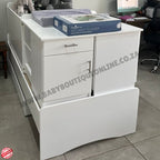 White baby changing table with drawers and a box on top, in an indoor setting.Babybedroominabox5-in-1Cot