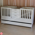 White baby twin crib with drawers on a wooden floor