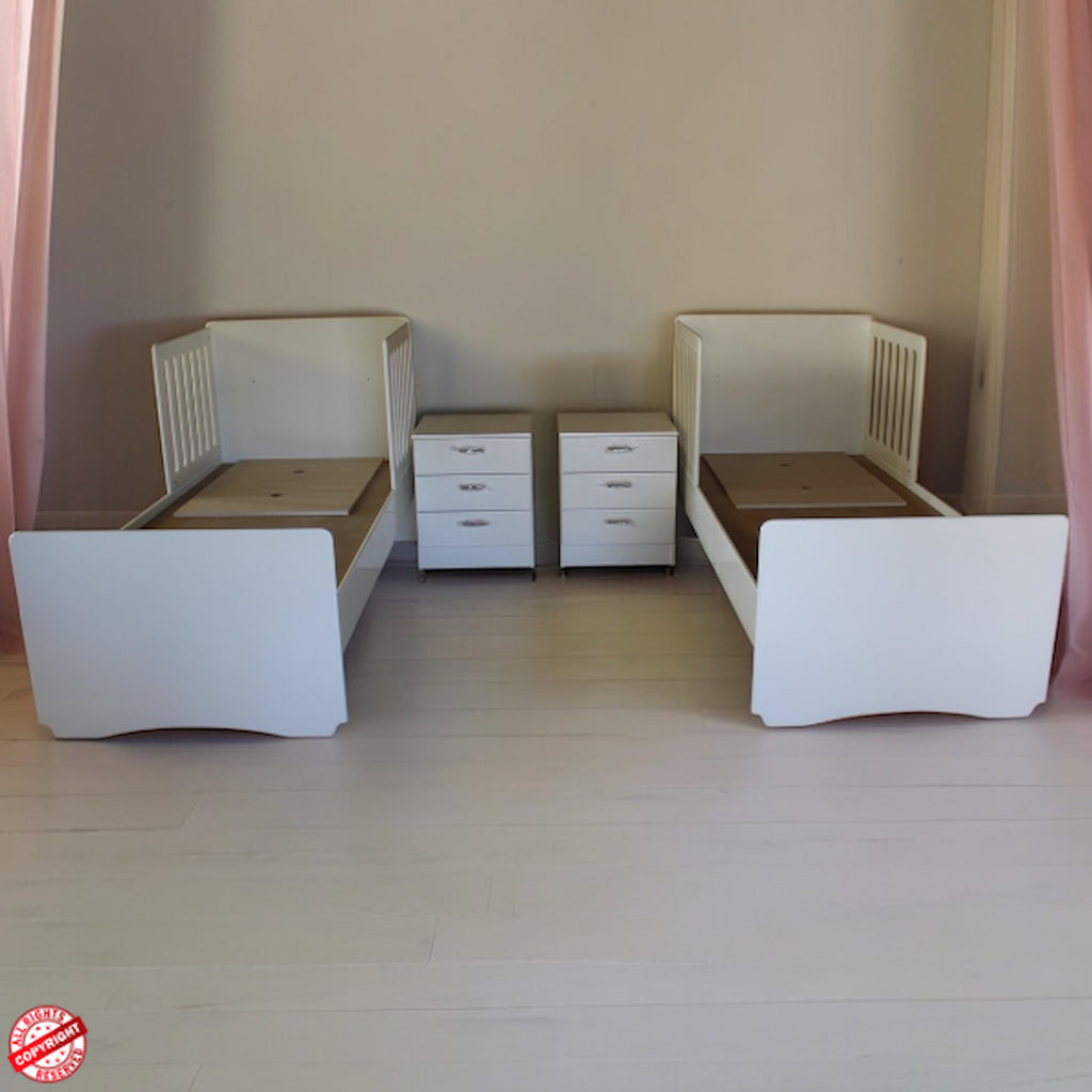 Two white children's beds with drawers in a room with pink curtains.