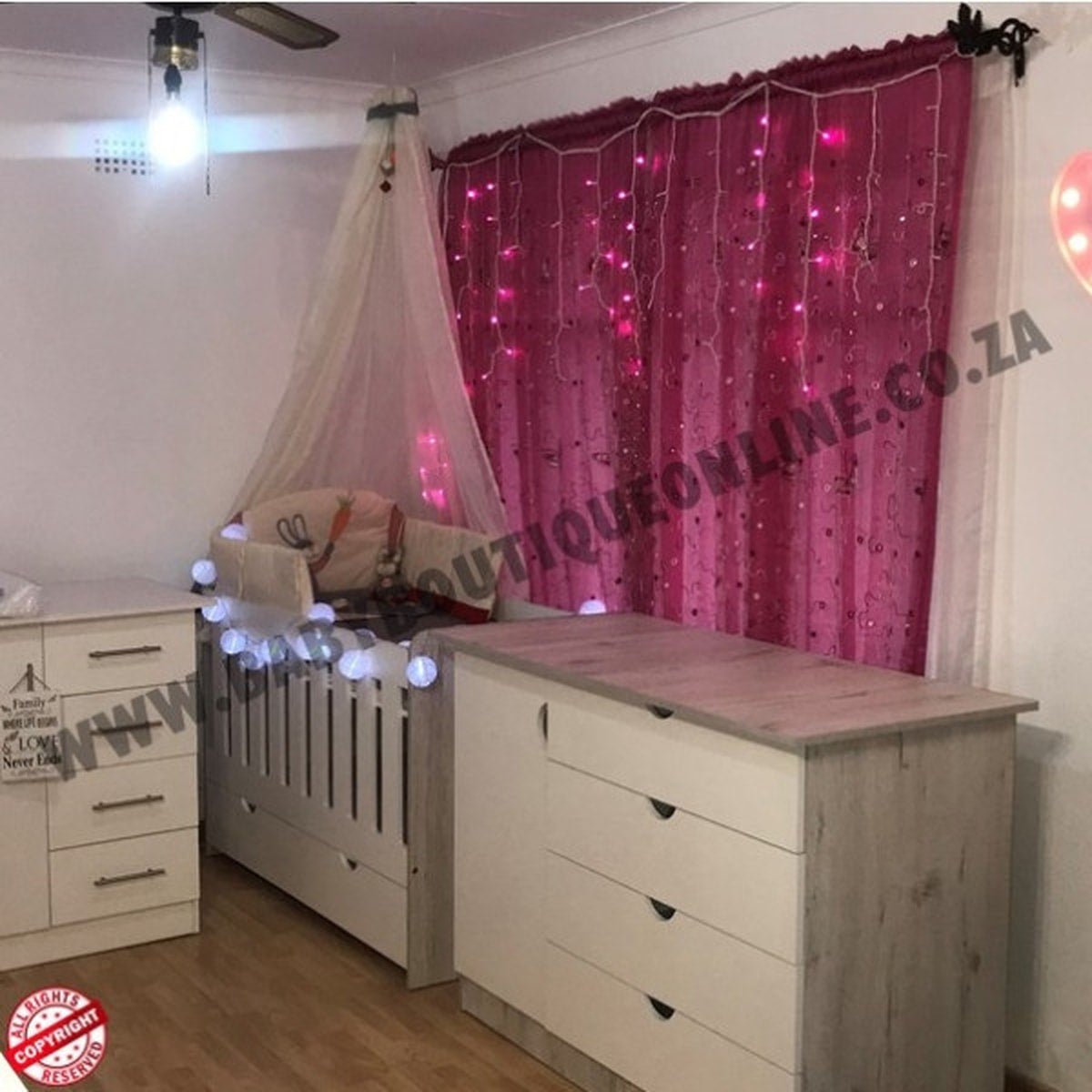 Children's room with crib, dresser, and pink curtain with lights.
