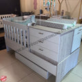 White baby crib with drawers and changing table in a showroom setting.