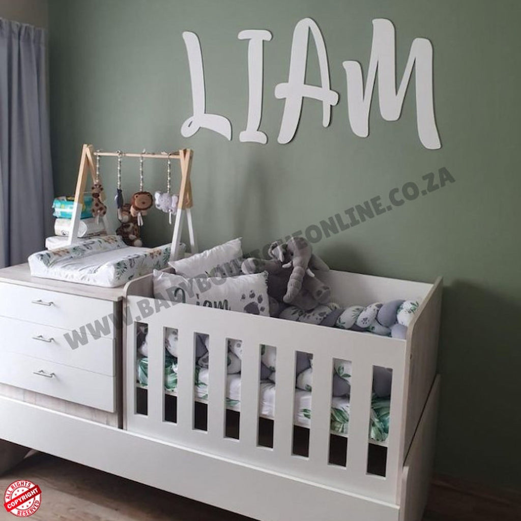 Nursery room with a crib, changing table, and toys against a green wall with 'LIAM' on it.