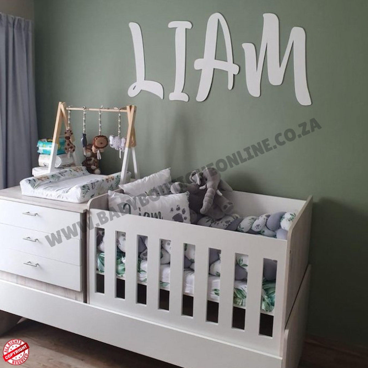 Nursery room with a crib, changing table, and toys against a green wall with 'LIAM' on it.