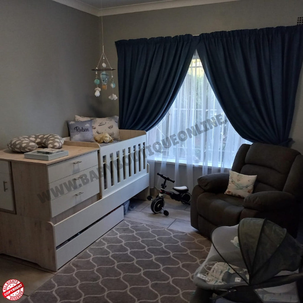Nursery room with crib, dresser, and chair near a window with dark curtains.