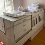 Wooden changing table with drawers and a small bed in a nursery setting.