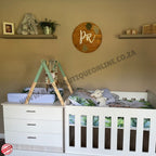 Nursery room with white crib, changing table, and decorative elements on a beige wall.