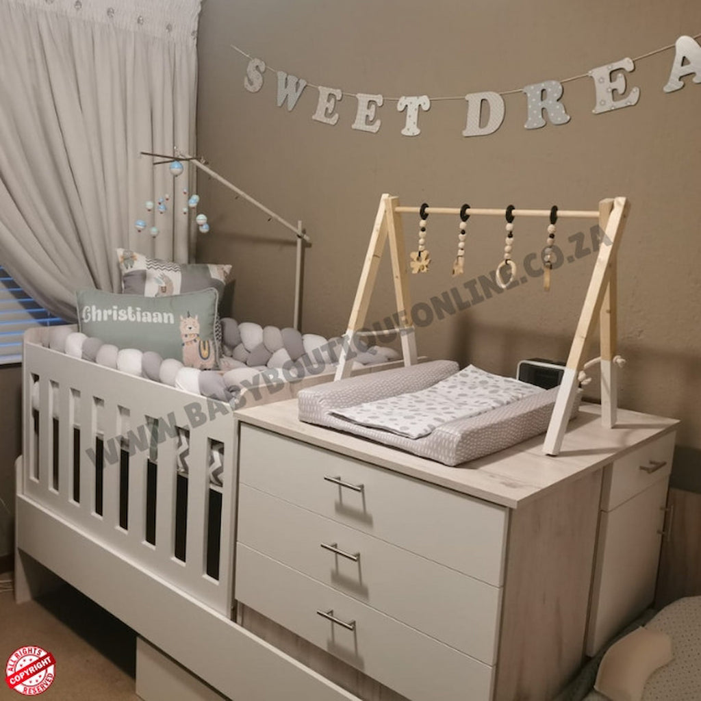 Baby nursery with crib, changing table, and decorative elements on a beige wall.