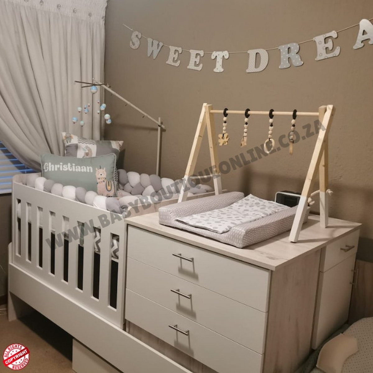 Baby nursery with crib, changing table, and decorative elements on a beige wall.