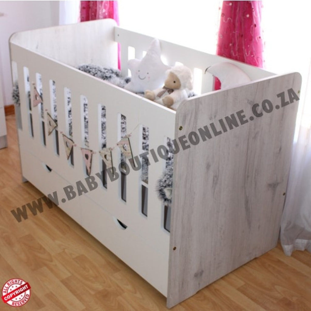 LargeWoodenCotwithSplitDrawerWhite_NordiC with toys inside, branded 'Baby Boutique Online.co.za', on a wooden floor.