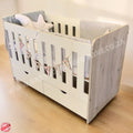 LargeWoodenCotwithSplitDrawerWhite_NordiC with wooden sides and gray bedding on a light wooden floor.