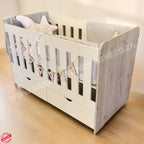 LargeWoodenCotwithSplitDrawerWhite_NordiC with wooden sides and gray bedding on a light wooden floor.