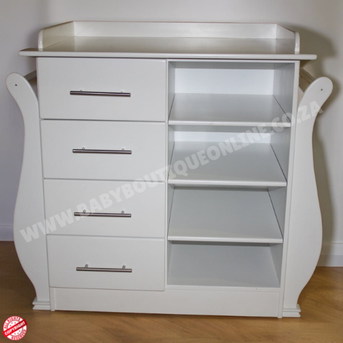 White baby changing table with drawers and shelves on a wooden floor.
