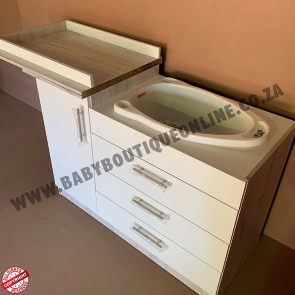 Baby changing station with sink and drawers against a beige wall.