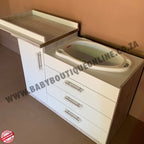 Baby changing station with sink and drawers against a beige wall.