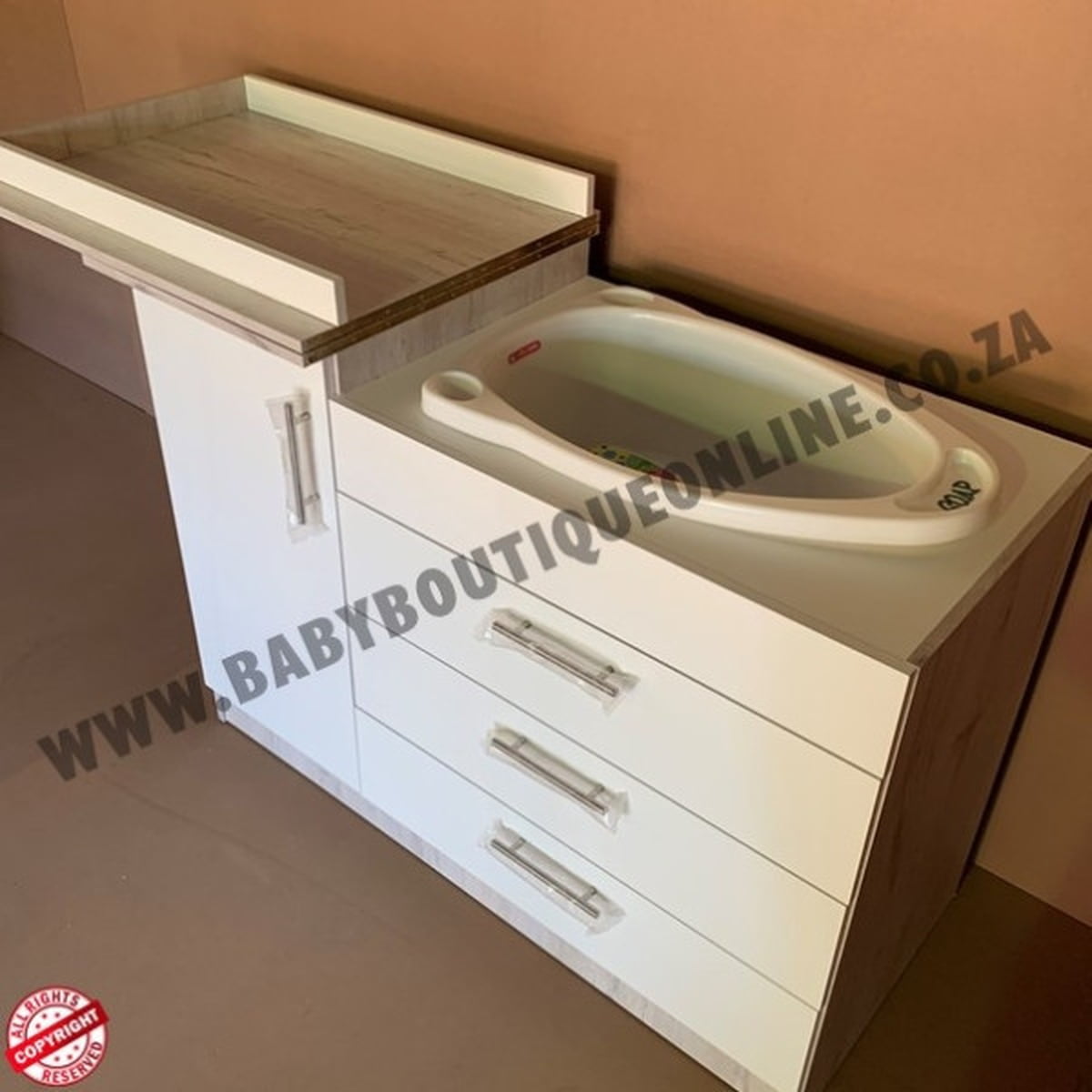 Baby changing station with sink and drawers against a beige wall.