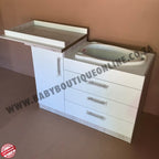White baby changing table with drawers against a beige wall.