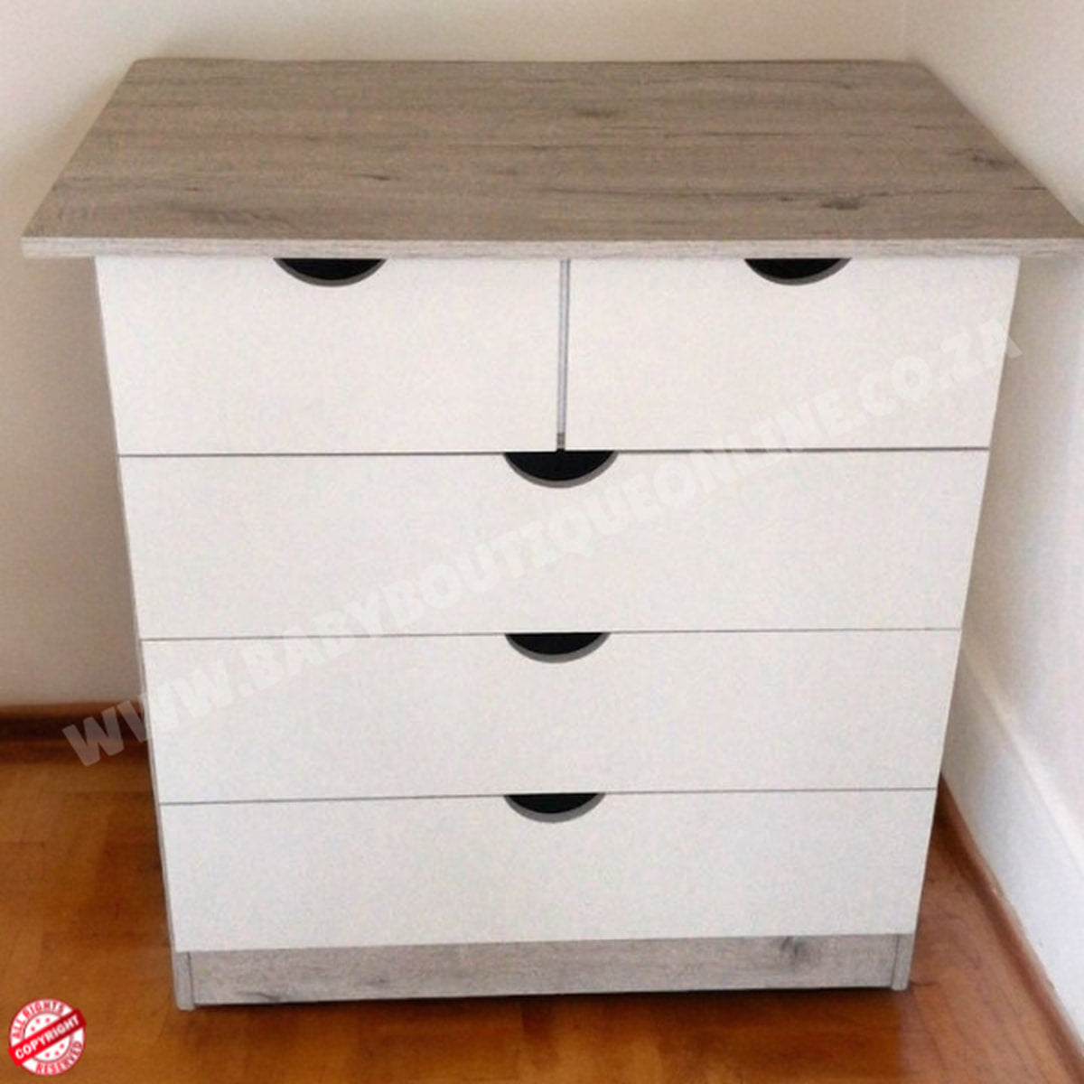 White dresser with gray top on a wooden floor against a white wall
