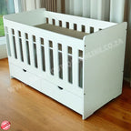 Large Wooden Cot with split Drawer-HalfMoon Cut Outs White crib with gray mattress on a wooden floor, brand logo visible