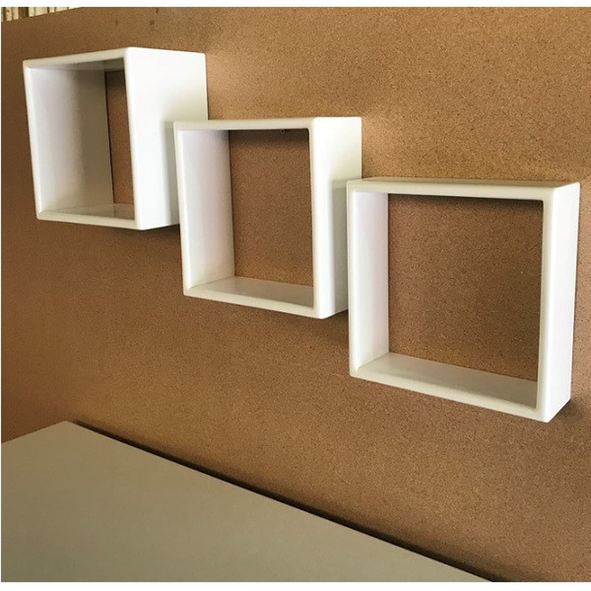 Three white square shelves on a brown wall