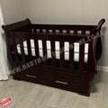 Sleigh Cot with Drawers Mahogany with drawers on a light wooden floor against a white wall.