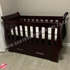 Sleigh Cot with Drawers Mahogany with drawers on a light wooden floor against a white wall.