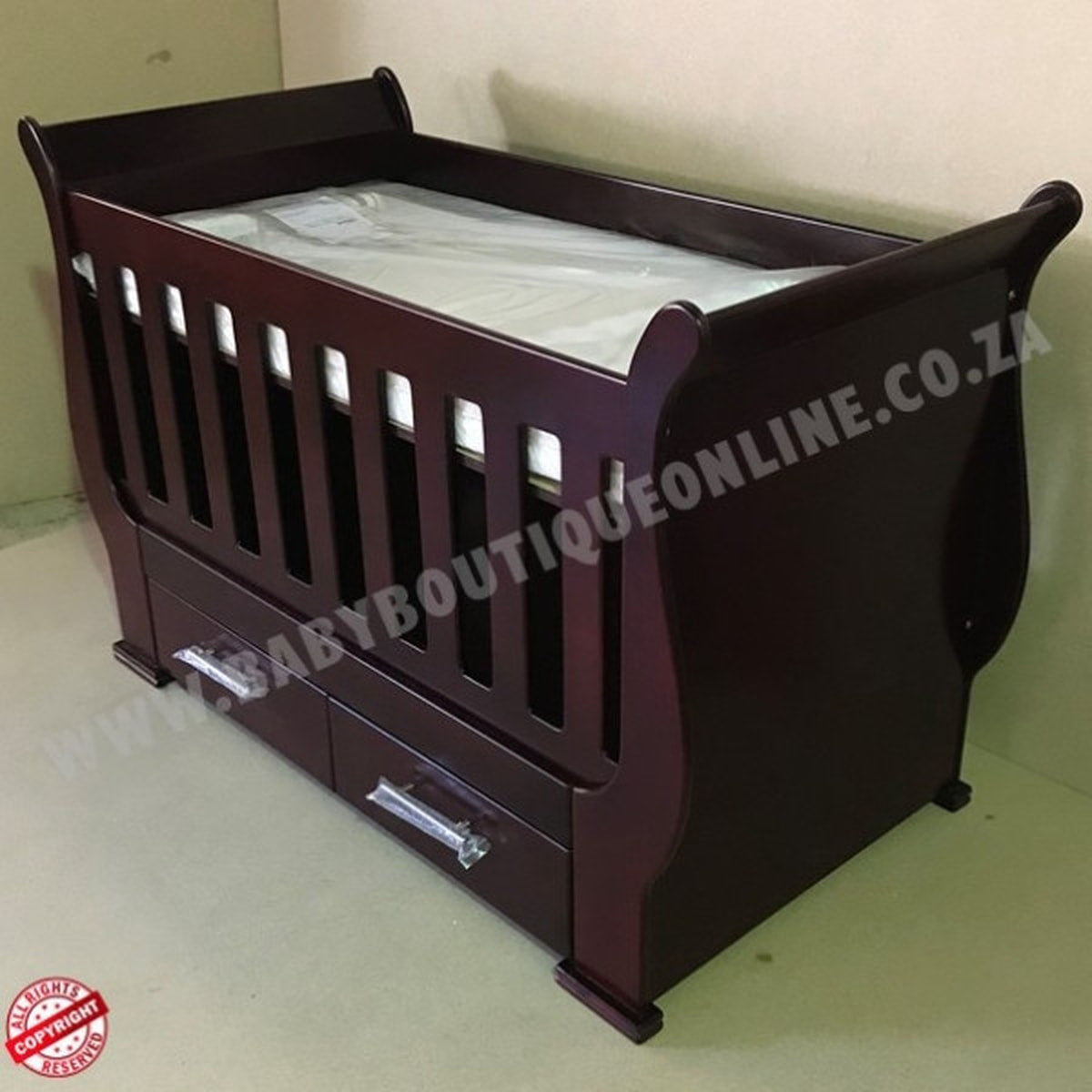 Sleigh Cot with Drawers Mahogany with drawers on a light wooden floor against a white wall.