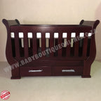 Sleigh Cot with Drawers Mahogany with drawers on a light wooden floor against a white wall.