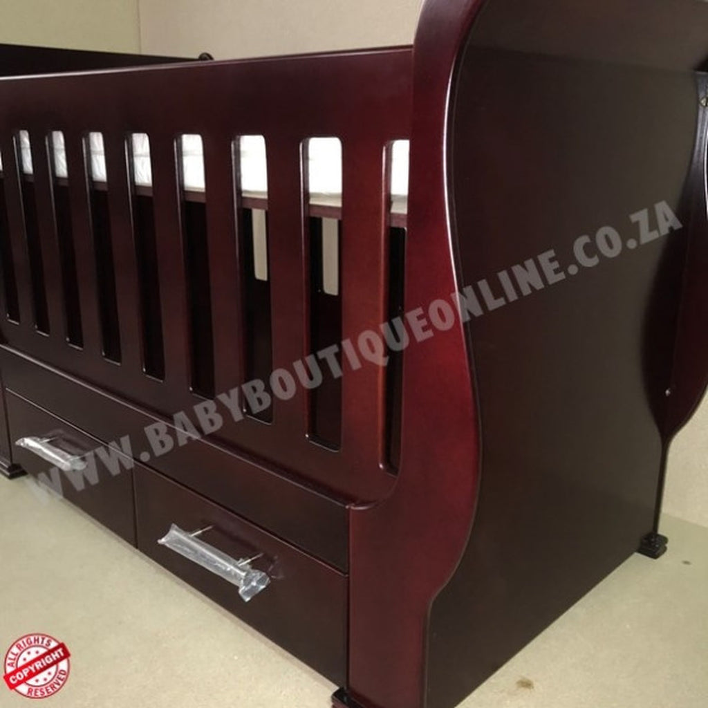 Sleigh Cot with Drawers Mahogany with drawers on a light wooden floor against a white wall.