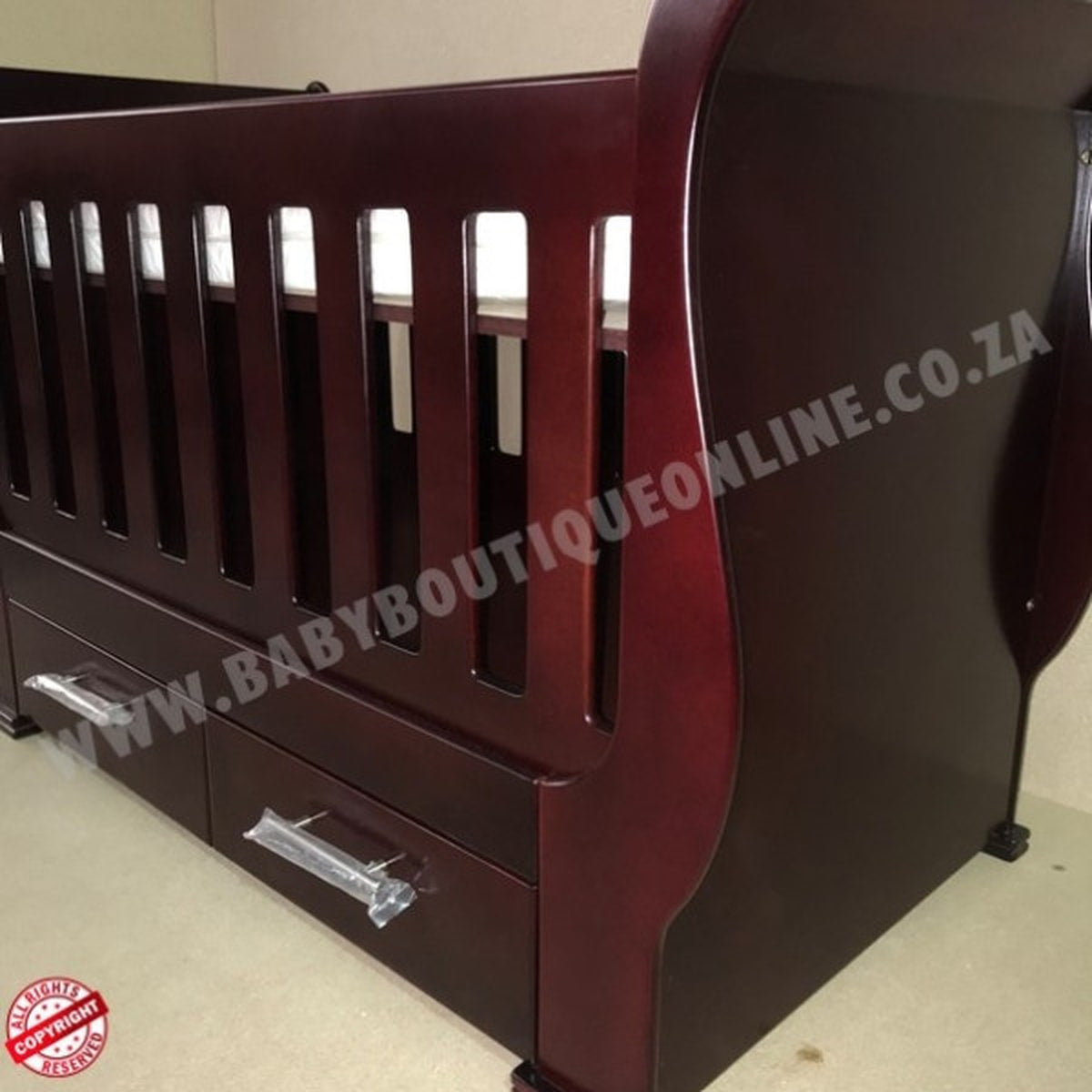 Sleigh Cot with Drawers Mahogany with drawers on a light wooden floor against a white wall.