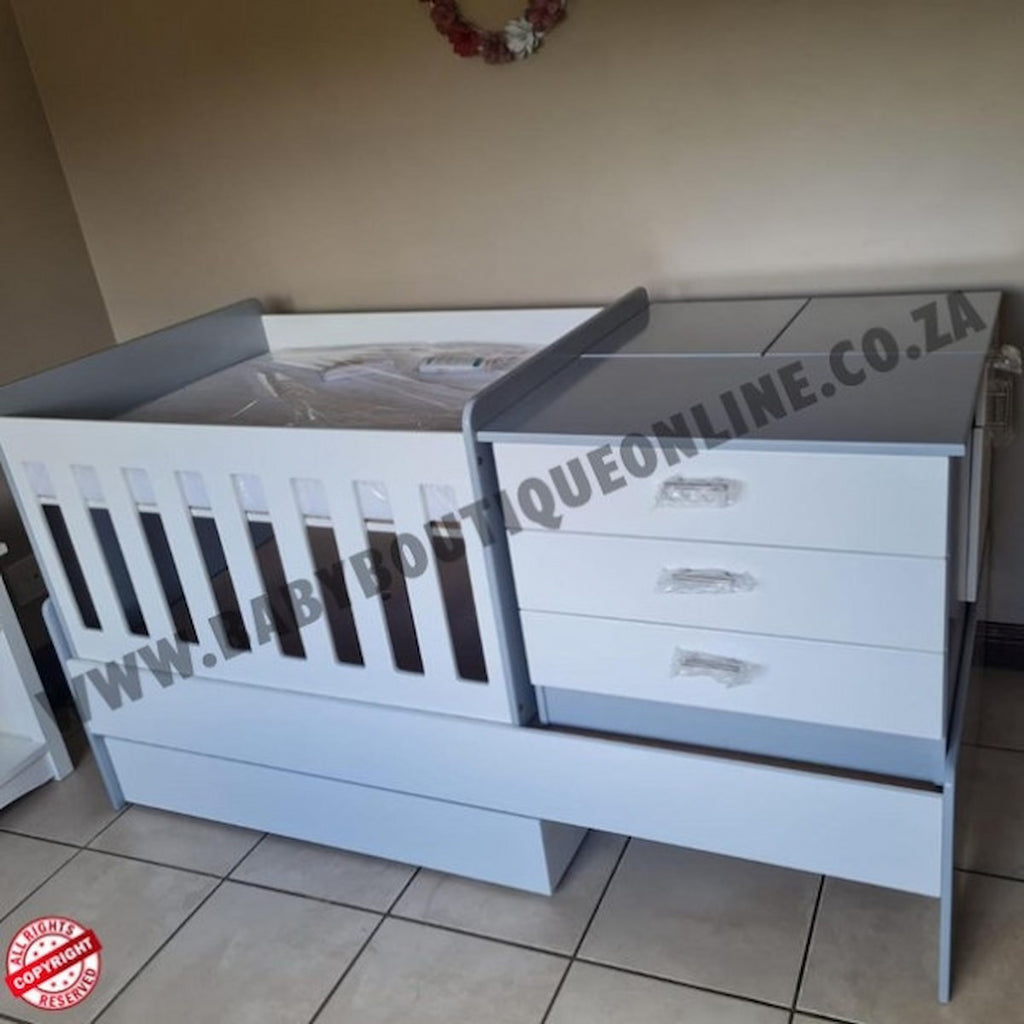 BabyBedroominaBox5-in-1Cot White crib with gray top and drawers on a tiled floor.