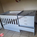 BabyBedroominaBox5-in-1Cot White crib with gray top and drawers on a tiled floor.