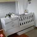 Bedroominabox-5-in-1Cot White baby crib with drawers and toys in a room setting.