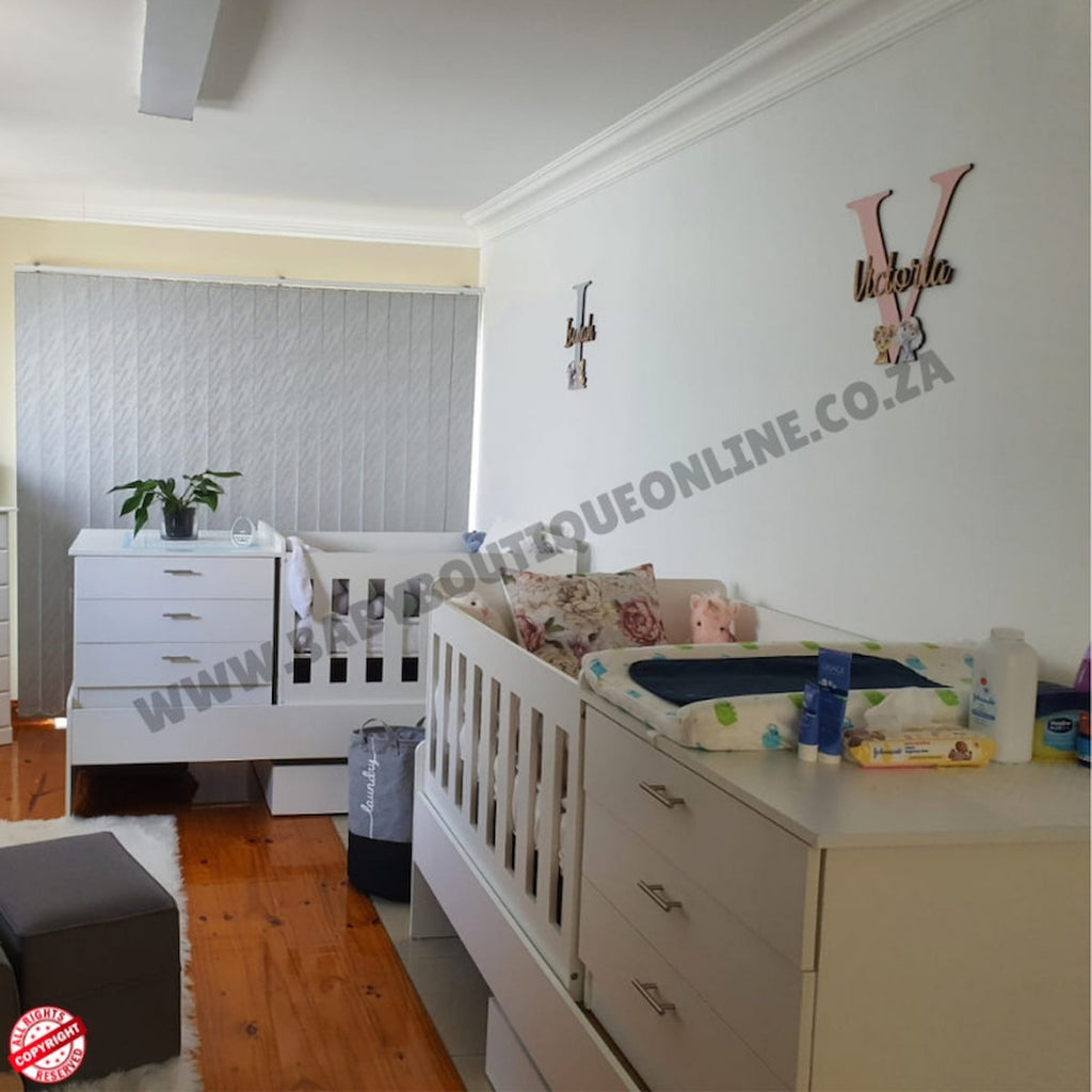 Children's bedroom with Bedroominabox-5-in-1Cot white crib, dresser, and toys on a wooden floor.